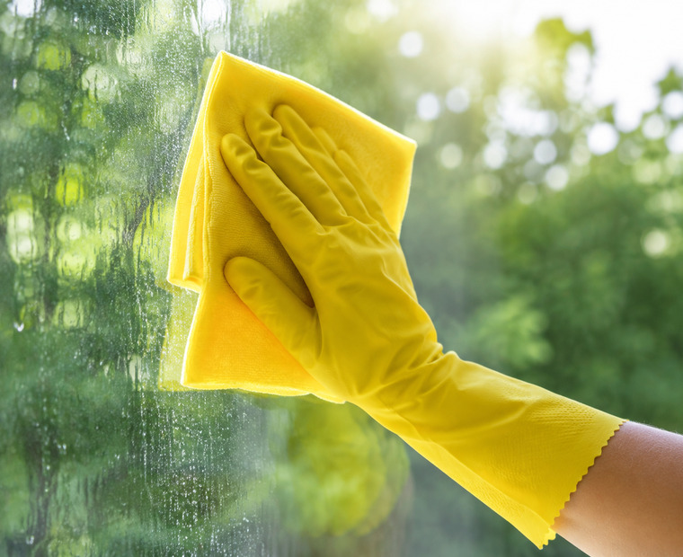 Hand in gelbem Handschuh wischt über eine Fensterscheibe